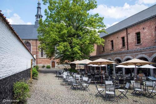 a patio with chairs and umbrellas in front of a building at Gîte de La Blanche Ferme près de Pairi Daiza in Lessines