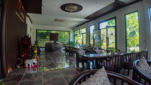 ein Esszimmer mit Tischen und Stühlen und Fenstern in der Unterkunft Lodge Moni Essara Kampot in Kampot