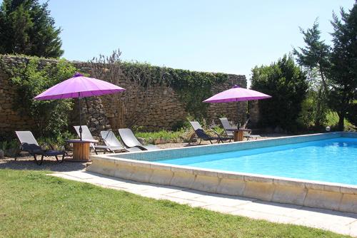 - une piscine avec 2 parasols, des chaises et une table avec des parasols dans l'établissement Maison d'hôtes Ferme de la Commanderie, à Richerenches