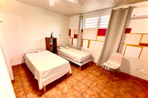 a bedroom with two beds and a window and a chair at Charmant T3 en RDJ chez Ketty à Ducos in Ducos