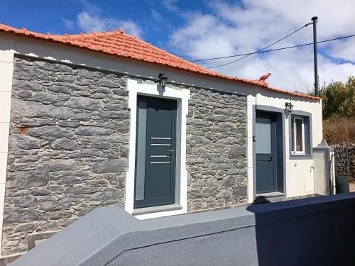 un cottage in pietra con porte blu e un muro di pietra di Adelaide's Cottage a Ponta do Pargo