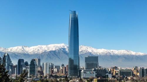Un rascacielos alto frente a una ciudad con montañas cubiertas de nieve. en Departamento Coyancura, en Santiago