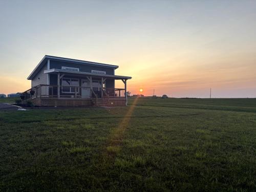 a house in a field with the sunset in the background at Down East Cabins in Tracadie