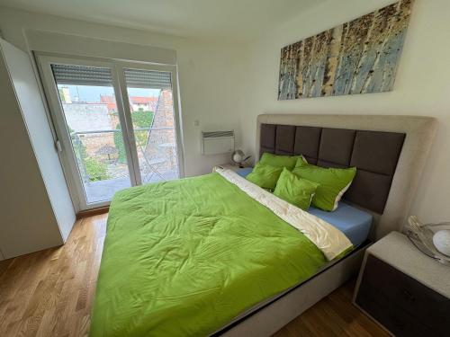 a bedroom with a bed with green sheets and a window at Julija 4 in Pančevo