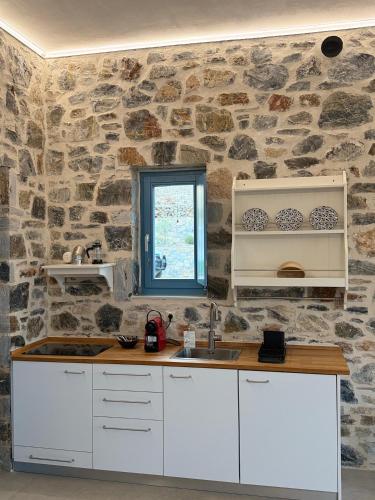 a kitchen with white cabinets and a stone wall at Filotimia in Schinoussa