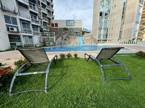 two chairs sitting in the grass near a swimming pool at Comodo departamento cerca de Costera Acapulco in Acapulco