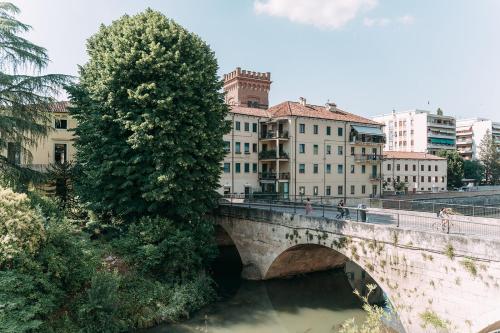 a bridge over a river with a tree and buildings at Palladio Apartment - Vista Fiume, In Centro con Garage in Vicenza