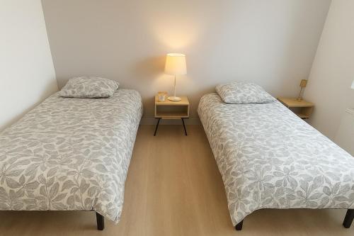 two beds in a room with a lamp on a table at La longère des cerisiers 