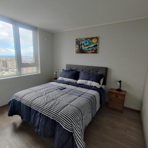 a bedroom with a bed with a striped comforter and two windows at Vanguardia 924 in Temuco