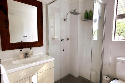 a white bathroom with a shower and a sink at On The Jetty Lake-view Apartment in Long Jetty