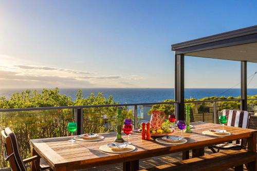 a wooden table with wine glasses on a balcony at Martha's Maison Heated Spa & Unbeatable Bay Views in Safety Beach