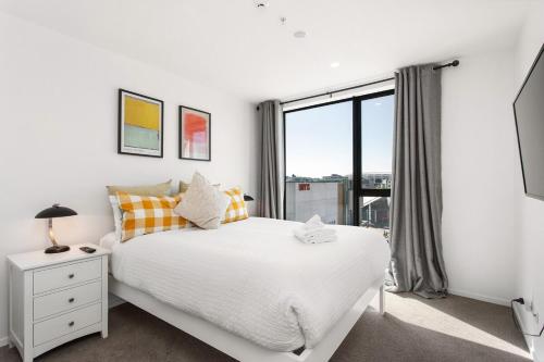 Un dormitorio con una cama blanca y una ventana grande. en Live the High Life 1 Bdrm Luxury With Park, en Christchurch