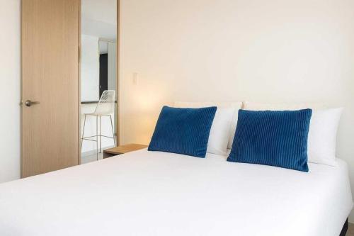 Una cama blanca con dos almohadas azules encima. en Apartaestudio cerca centros comerciales -Refugio romantico, en Ibagué