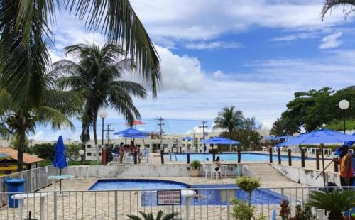 a pool with palm trees and blue umbrellas at Comfort and good memories, right by the lagoon! in São Pedro da Aldeia
