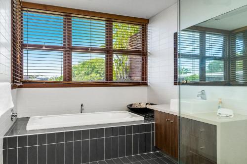a bathroom with a tub and a sink and windows at A Seventh Heaven - 6 21- 25 Fletcher Street in Byron Bay