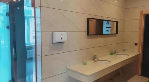 a bathroom with two sinks and a television on the wall at GreenTree Inn Yichun Qingshan Street Express Hotel in Jiamusi