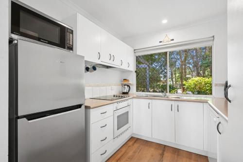 a kitchen with white cabinets and a large window at 2 Bedroom Ground Level Villa in Tropical 4* Resort in Noosaville
