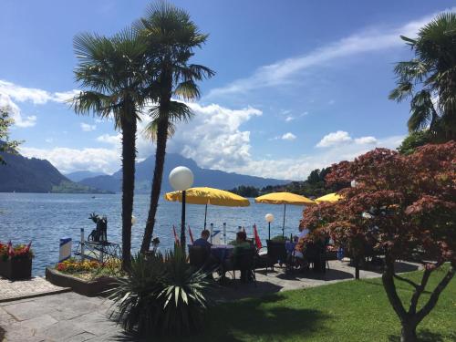 a group of people sitting at a table with umbrellas by the water at Hotel Beau Rivage Weggis in Weggis