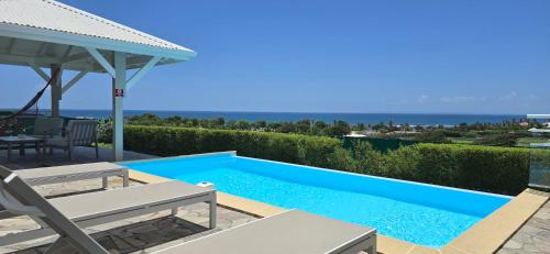 サン・フランソワにあるLes villas "Fenêtres Sur Plage" - Villas Créoles de charme , vue exceptionnelle face mer et plage & piscines privées à débordementの青いスイミングプール(テーブル、椅子付)