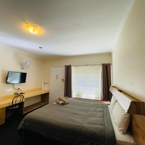 a bedroom with a bed with a desk and a window at Wee Waa Motel in Wee Waa