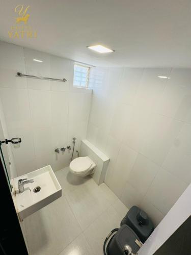 a white bathroom with a toilet and a sink at Hotel Yatri in Gandhinagar