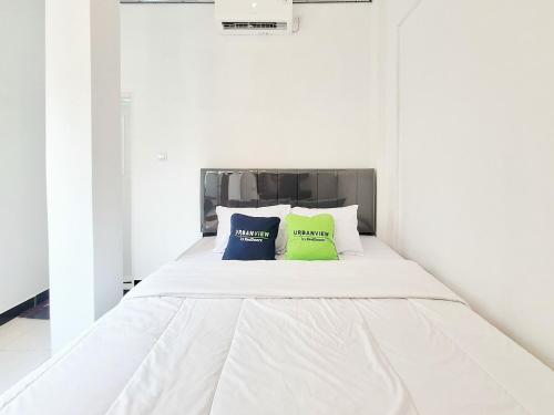 a white bed with two blue and green pillows on it at Urbanview Bimo Homestay near Sindu Kusuma Edupark Yogyakarta in Jetis