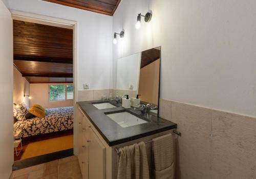 une salle de bain avec un lavabo, un miroir et un lit dans l'établissement Casa Capelas, à São Vicente Ferreira