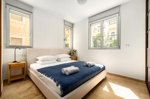 a bedroom with a bed with blue sheets and windows at Gordon Beach Bright Spacious Stay in Tel Aviv