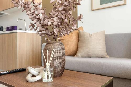 Un jarrón con flores en una mesa junto a un sofá. en Silkhaus Deluxe 1BR in Masdar City at Oasis, en Abu Dhabi Intl