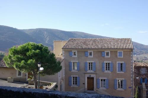 Una casa grande con un árbol y montañas al fondo. en Le Chef d'Escadron, en Bonnieux
