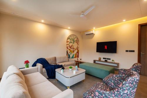 a living room with a couch and chairs and a tv at SaffronStays Pebble House - 3BR riverside villa with glass walls, terraces & Nun River views, Dehradun in Dehradun