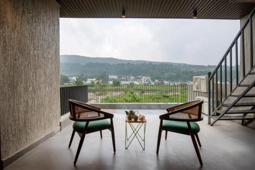 two chairs and a table on a balcony with a view at SaffronStays Pebble House - 3BR riverside villa with glass walls, terraces & Nun River views, Dehradun in Dehradun
