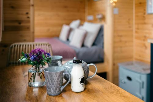 a wooden table with two cups and a vase of flowers at Shepherd's Huts in Barley Meadow at Spring Hill Farm in Oxford