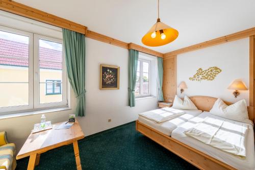 a bedroom with a bed and a table and windows at Hotel Krug in Gumpoldskirchen