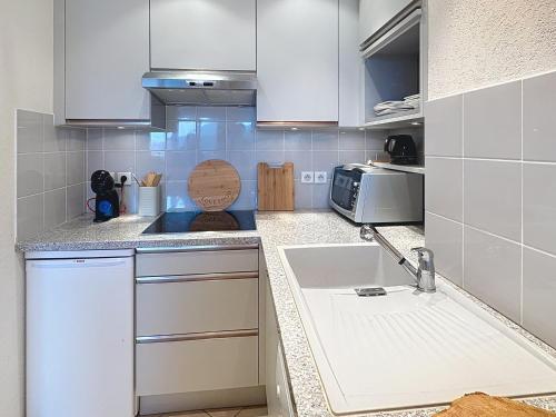 a kitchen with white cabinets and a sink at Cocon moderne vue pistes - Balcon sud- télécabine 160 m in Chamrousse