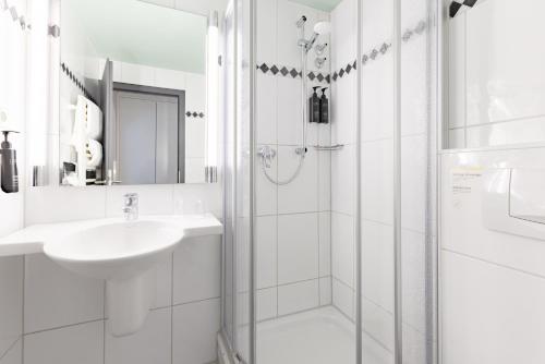 Un baño blanco con lavabo y ducha. en Garner Hotel Cologne East by IHG, en Colonia