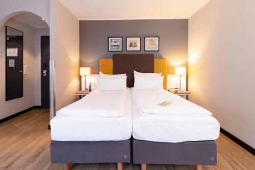 two beds in a hotel room with white sheets at Garner Hotel Cologne East by IHG in Cologne