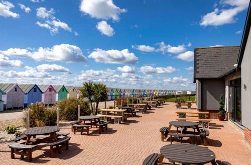a row of picnic tables and benches in front of beach houses at Cosy Little Home By The Sea in West Mersea