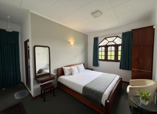 een slaapkamer met een bed, een spiegel en een stoel bij Kings Villa Nuwara Eliya in Nuwara Eliya
