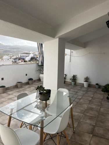 a glass table and white chairs on a balcony at La terraza de la subbética in Luque