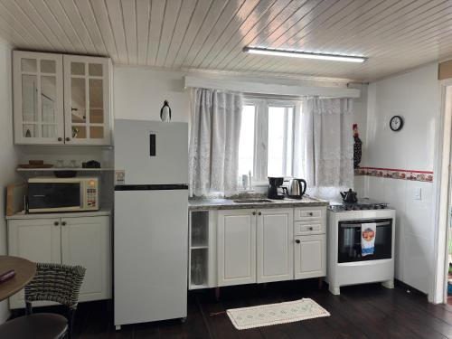 Una cocina con gabinetes blancos y un refrigerador blanco. en Estúdio casa condomínio Carasol, en Caraguatatuba