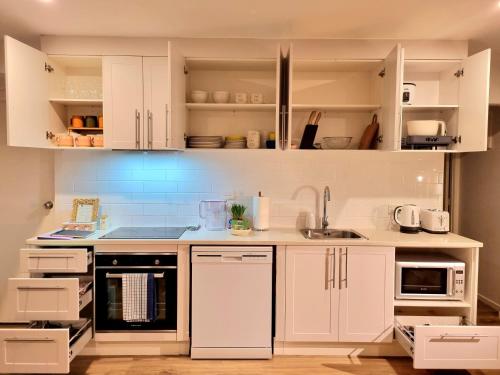a white kitchen with white cabinets and appliances at Train, Zoo & Eden Park Nearby - Arcade, Disney Plus- Free Parkings- Central & Peaceful in Auckland