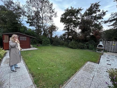 uma mulher parada no quintal de um quintal em Ruhiger Bungalow Nr 156 "Haus Gezellig" Strandnah mit großen, uneinsehbaren Garten, am Ende des Parks, sehr ruhig em Sint Maartenszee