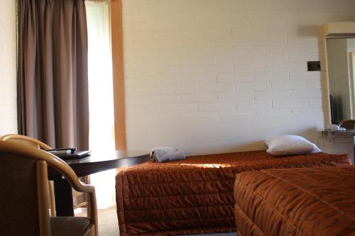a hotel room with two beds and a desk and a table at Cobram Colonial Motor Inn in Cobram