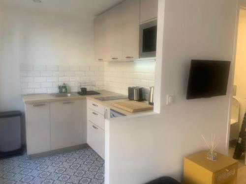 a kitchen with white cabinets and a tv on the wall at La petite Catène in Le Havre