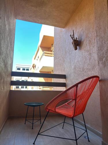 ein roter Stuhl und Hocker auf einem Balkon mit einem Fenster in der Unterkunft Luxury Central Apartment Marrakech Pool Near train station in Marrakesch