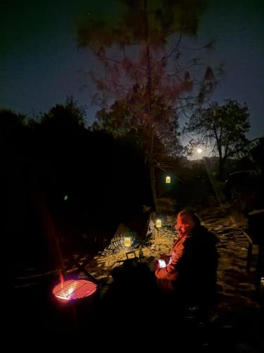 a man sitting next to a camp fire at night at Rocky Ridge Glamping Yosemite in Coarsegold