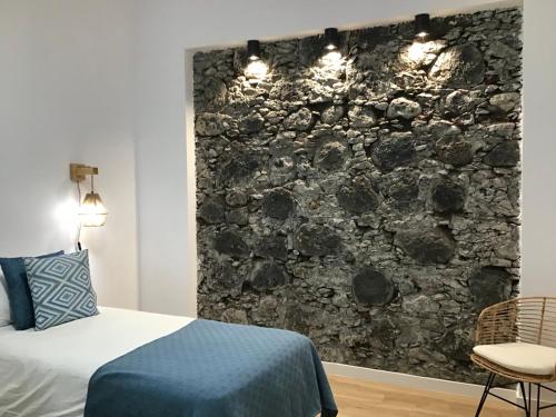 1 dormitorio con pared de piedra, cama y silla en Casa Garnier, en Santa Cruz de la Palma
