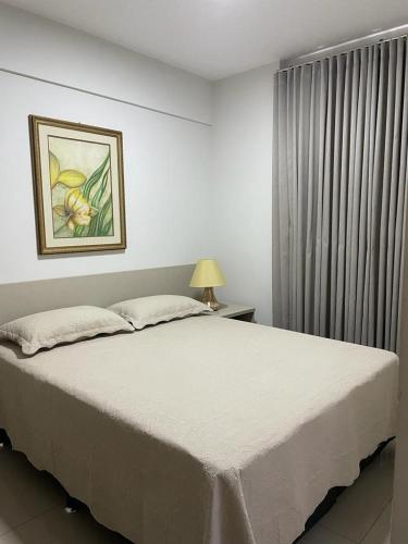 a bedroom with a white bed with a picture on the wall at Park Veredas Apto 334 in Rio Quente