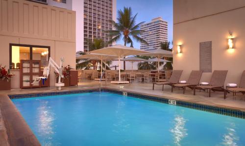 a swimming pool with chairs and umbrellas next to a building at Hyatt Place Waikiki Beach in Honolulu